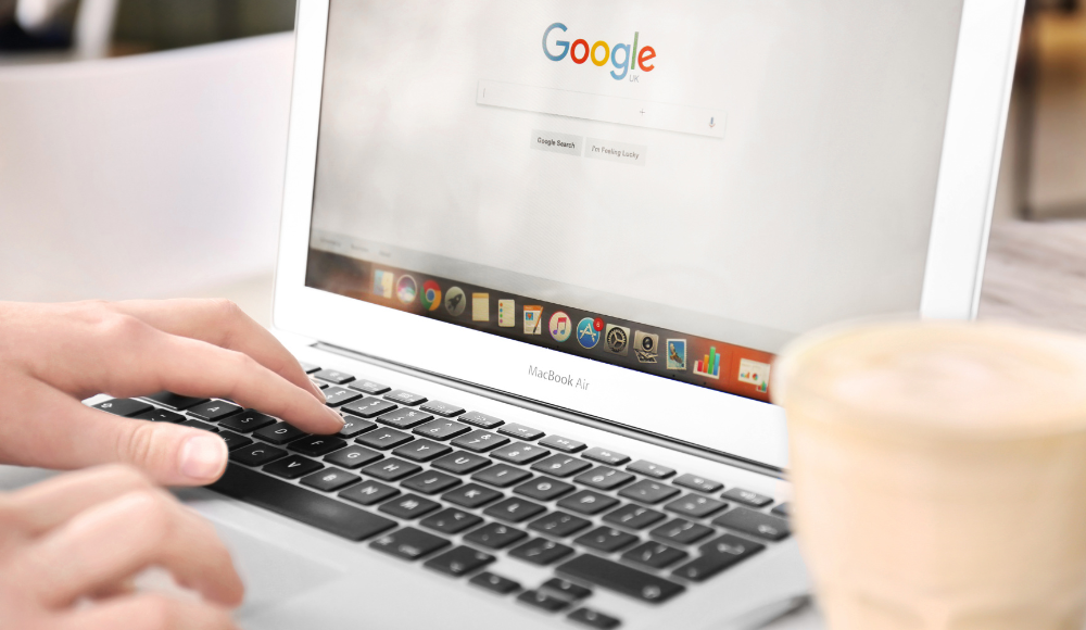Person using a MacBook Air to search on Google, emphasizing the power of Google Ads for local businesses, with a coffee cup nearby.
