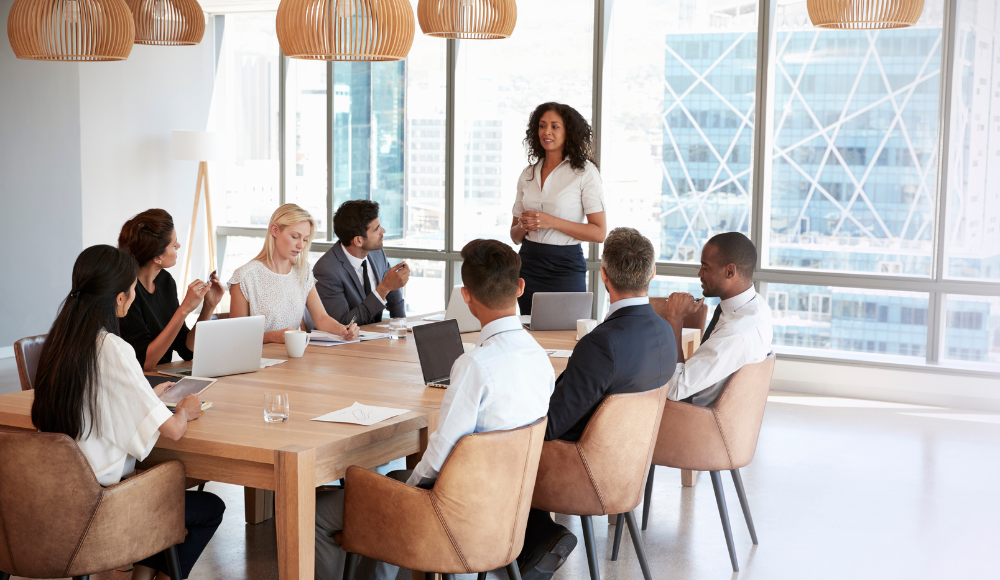 Diverse business team in a modern meeting room, with one person presenting to colleagues during a discussion.
