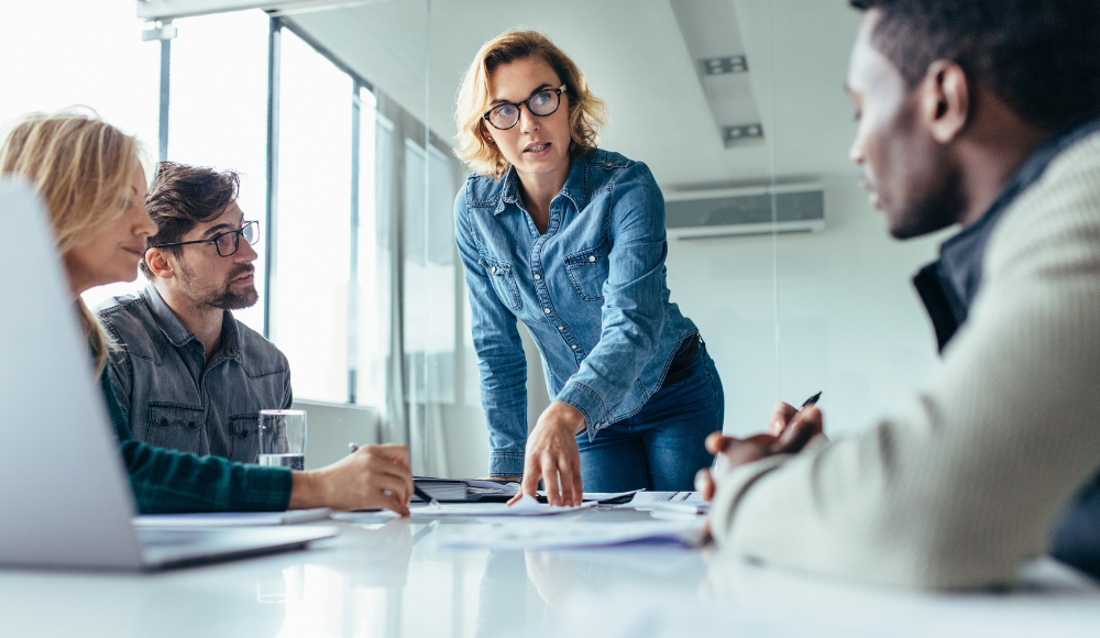 Businesswoman leading a team meeting and explaining documents to colleagues around a conference table in a bright office.
